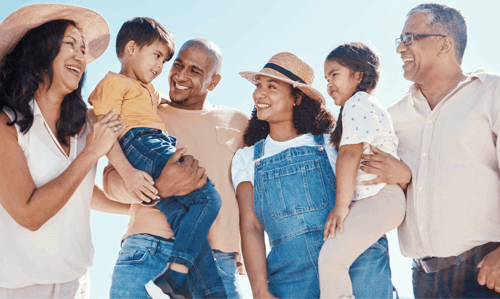 Grandparents, kids, and grandkids smiling together in a sunny outdoor setting.